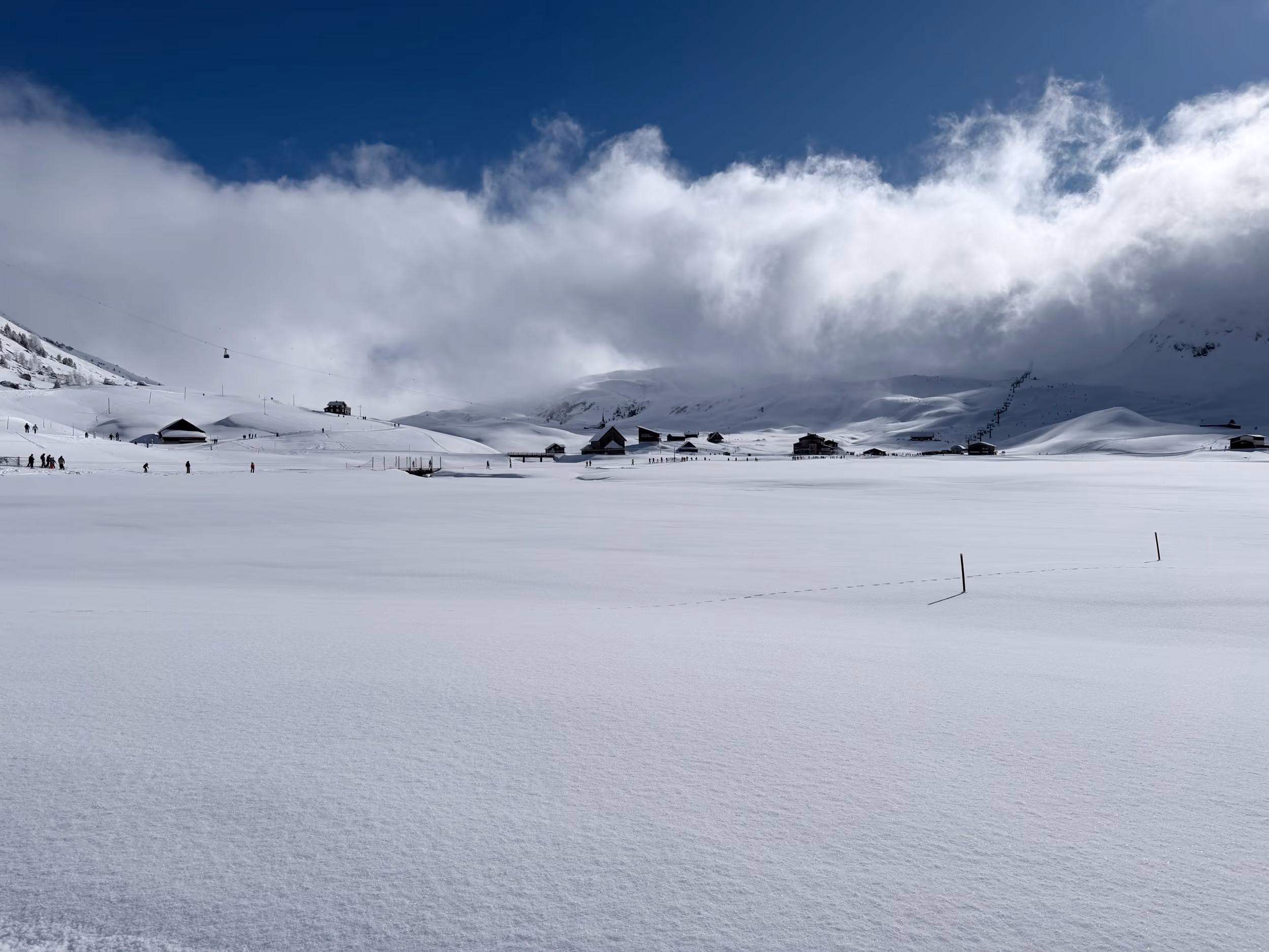 Weite Schneefläche über dem Melchsee, dahinter Alphütten und Wolken über den Bergen