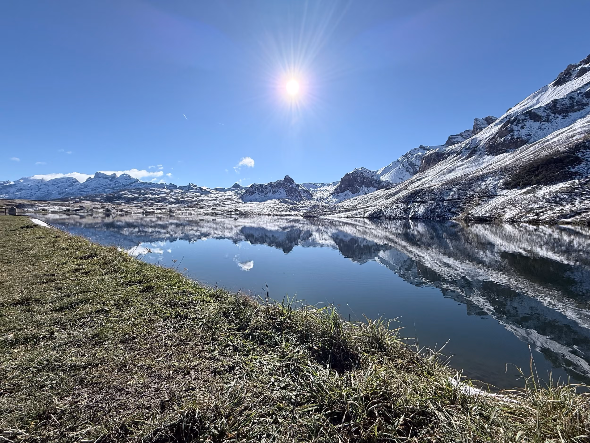 Der Melchsee spiegelt die frisch verschneiten Berge, am Ufer grünes Gras